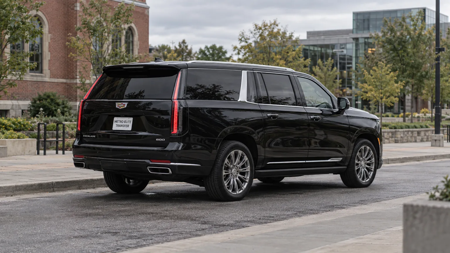 A black Cadillac Escalade ESV with a Metro Elite Transfer plate in a brick and modern university-district setting