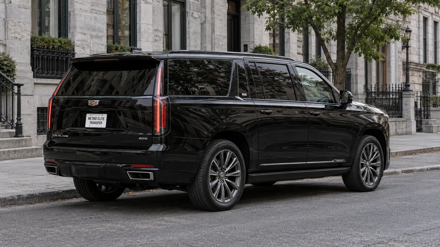 A black Cadillac Escalade ESV with a Metro Elite Transfer plate in a limestone-lined city street
