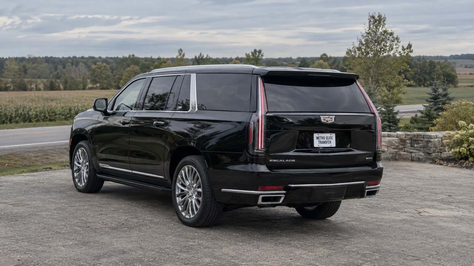 Black Cadillac Escalade ESV parked in a roadside pull-off beside a quiet rural landscape